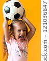 Authentic cute smiling preschool little girl with classic black and white soccer ball look at camera on yellow background. child play football in t-shirt and shorts. Sport, championship, team concept 121036847