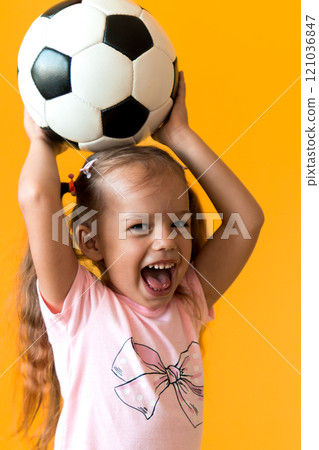Authentic cute smiling preschool little girl with classic black and white soccer ball look at camera on yellow background. child play football in t-shirt and shorts. Sport, championship, team concept Authentic cute smiling preschool little girl with classic black and white soccer ball look at camera on yellow background. child play football in t-shirt and shorts. Sport, championship, team concept 121036847