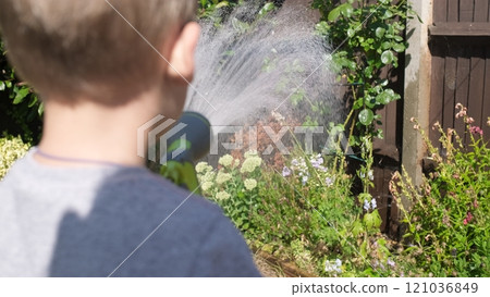 Funny little boy watering lawn plants in garden housing backyard. Adorable child playing with irrigation hose at hot sunny summer outdoors. Children help with housework. activity for kids. Childhood Funny little boy watering lawn plants in garden housing backyard. Adorable child playing with irrigation hose at hot sunny summer outdoors. Children help with housework. activity for kids. Childhood 121036849