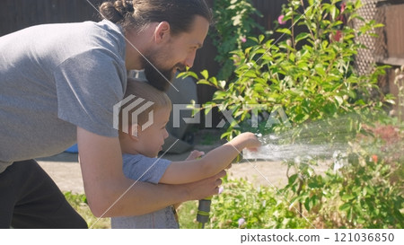 Father and Son. Funny little boy watering lawn plants in garden housing backyard with Dad. Summer house work. Hardworking preschool Kid outdoors. Children help with housework. activity for kids 121036850
