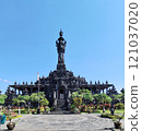 Visitors walking along the pathway toward the Bajra Sandhi Monument in Denpasar, Bali, surrounded by vibrant green trees and sunny weather 121037020