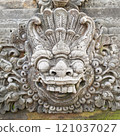 A beautifully crafted traditional Balinese monument adorned with detailed stone carvings, set against a clear blue sky and surrounded by local architecture. 121037027