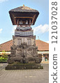 A beautifully crafted traditional Balinese monument adorned with detailed stone carvings, set against a clear blue sky and surrounded by local architecture. 121037028