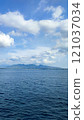 A tranquil tropical coastline with calm blue waters, distant hills, and ferry boats docked under a bright blue sky. 121037034