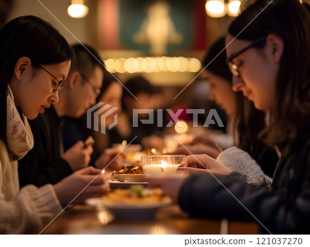 In a warm and inviting restaurant, friends gather around a wooden table, sharing a candlelit meal. 121037270