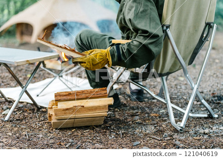 一名男性露營者在露營地點燃篝火的後視圖 一名男性露營者在露營地點燃篝火的後視圖 121040619