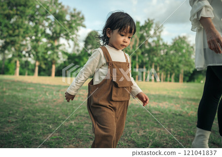 toddler baby girl walking with her mother in grass field 121041837