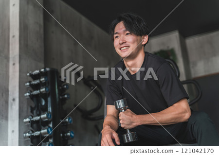 亞洲男子在健身房用啞鈴和鐵陣列進行肌肉訓練以加強手臂 亞洲男子在健身房用啞鈴和鐵陣列進行肌肉訓練以加強手臂 121042170