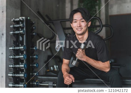 亞洲男子在健身房用啞鈴和鐵陣列進行肌肉訓練以加強手臂 亞洲男子在健身房用啞鈴和鐵陣列進行肌肉訓練以加強手臂 121042172