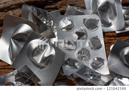 Empty blister packs scattered on wooden surface, highlighting waste and environmental concerns. image captures metallic texture and reflective surfaces of discarded packaging 121042599