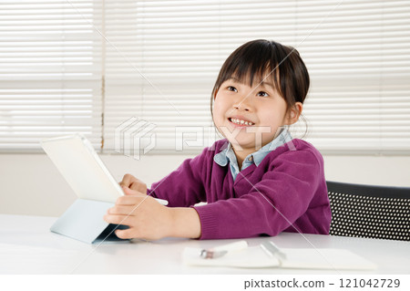 An elementary school girl who is confident in her studies is operating a tablet with a smile 121042729