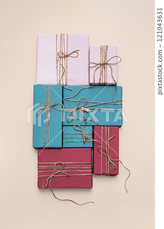 Various colorful gift boxes tied with rustic twine arranged on beige surface 121043631