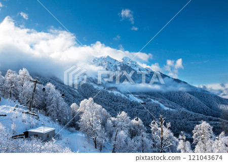 Snowy peaks of mountains above the clouds and gondola lift on a clear winter day 121043674