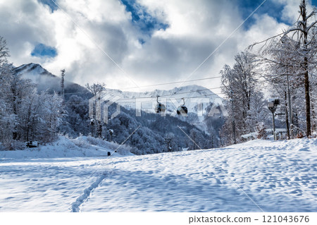 Snowy peaks of mountains above the clouds and gondola lift on winter day 121043676