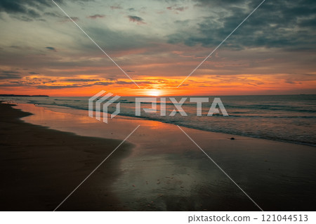 A serene coastal sunset over the ocean waves with vibrant sky colors and a peaceful atmosphere 121044513