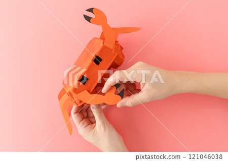 top down view of hands crafting DIY crab toy made from orange painted egg carton and paper cutouts. Step-by-step collage on a pink background. Craft project for kids, 121046038
