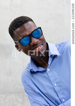 Smiling African American Man In His 40s With Blue Sunglasses And Shirt. Portrait Of Happy Stylish Middle Age Male, Gray Concrete On Background. Accessories. Vertical Plane 121046108