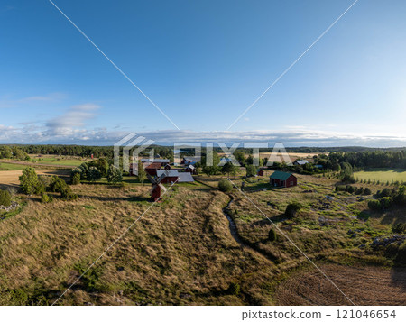 Tranquil charm of Aland Islands, Finland. Red farmhouses amidst fields and meadows framing a rustic windmill under a clear blue sky 121046654