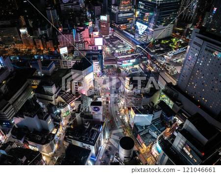 Aerial view of Shibuya crossing at night, Tokyo, Japan, illuminated by neon lights and vibrant billboards, surrounded by busy traffic and tall skyscrapers 121046661
