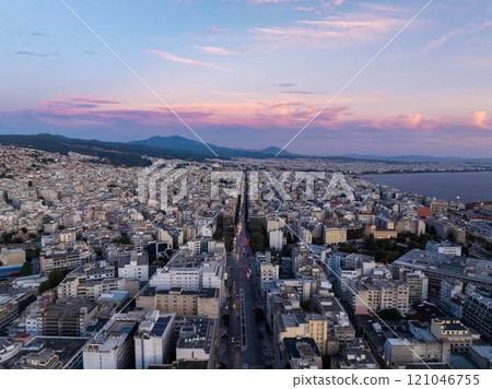 Aerial shot of Thessaloniki city center at sunset, with vibrant clouds above busy streets and tall buildings, overlooking the Thermaic Gulf in Greece 121046755