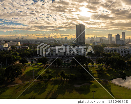 Aerial view of Manila cityscape with National Museum complex during sunrise under cloudy sky, showcasing urban skyline, green parks, and historical architecture 121046828
