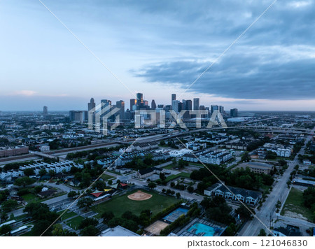 Aerial view capturing Houston's skyline at dawn with cold tones. Skyscrapers rising above a misty cityscape, highways, and neighborhoods set against a dramatic cloudy backdrop Aerial view capturing Houston's skyline at dawn with cold tones. Skyscrapers rising above a misty cityscape, highways, and neighborhoods set against a dramatic cloudy backdrop 121046830