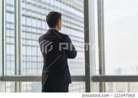 asian businessman standing by window looking at view 121047068