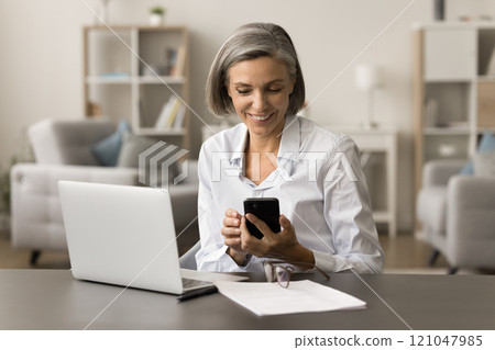 Cheerful senior freelance business woman typing on smartphone 121047985