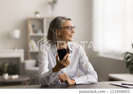 Cheerful grey haired business professional woman in glasses holding cellphone 121048003