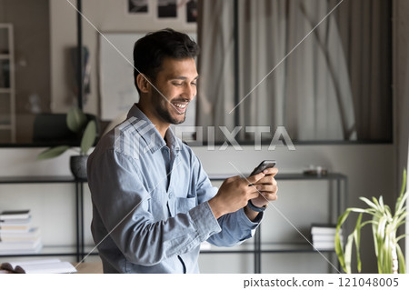 Satisfied Indian businessman using smartphone in office Satisfied Indian businessman using smartphone in office 121048005