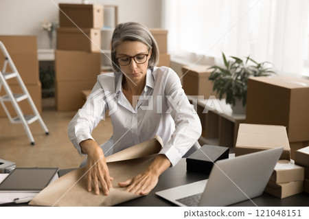 Serious mature storage employee wrapping small box Serious mature storage employee wrapping small box 121048151