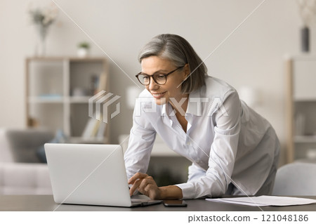 Positive busy grey haired business woman typing on laptop computer Positive busy grey haired business woman typing on laptop computer 121048186