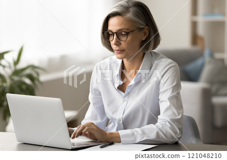 Focused mature business woman in elegant glasses typing on laptop Focused mature business woman in elegant glasses typing on laptop 121048210