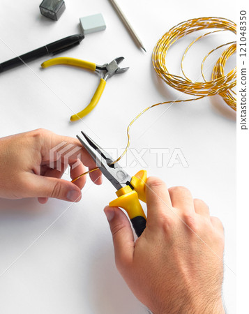 Hands using pliers to trim wire with tools on white surface for diy project Hands using pliers to trim wire with tools on white surface for diy project 121048350