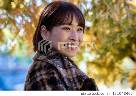 一位留著短鮑勃的年輕女子正在欣賞秋葉 121048402