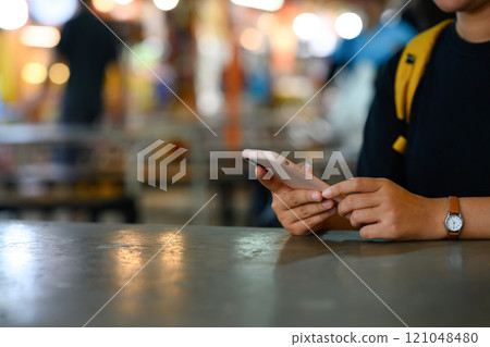 Close up of woman using smartphone at table in bustling night market with bright bokeh lights 121048480