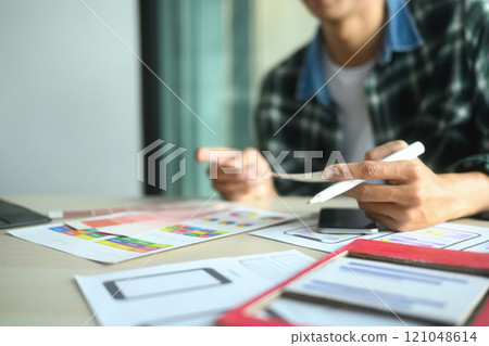 Designer analyzing color swatches and wireframe sketches while working on a project at desk Designer analyzing color swatches and wireframe sketches while working on a project at desk 121048614