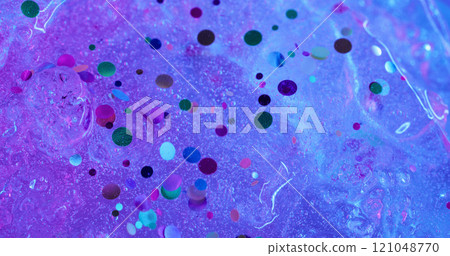 Shiny fluid. Confetti spill. Water with decorative sparks flows down purple ice surface. Festive colored defocused background with neon ink effect. 121048770