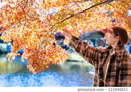一位留著短鮑勃的年輕女子正在欣賞秋葉 121048811