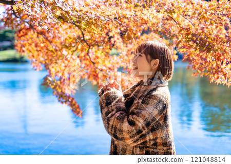 一位留著短鮑勃的年輕女子正在欣賞秋葉 一位留著短鮑勃的年輕女子正在欣賞秋葉 121048814