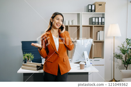Smiling Asian woman talking on the phone with a customer Young positive female accountant using smartphone talking Smiling Asian woman talking on the phone with a customer Young positive female accountant using smartphone talking 121049362