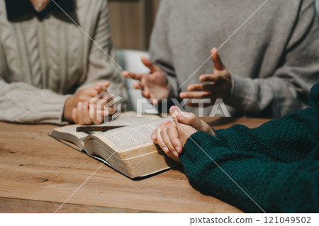 Group of Christians sit together and pray around a wooden table with blurred open Bible pages in their homeroom. Prayer for brothers, faith, hope, 121049502