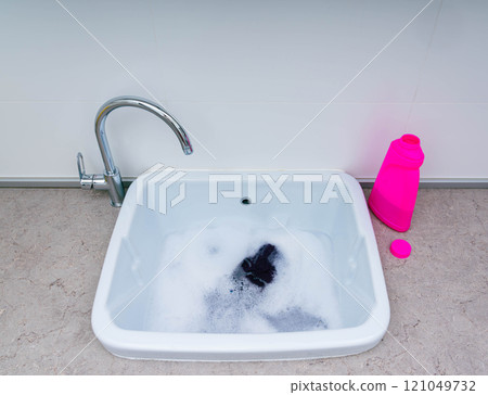 Washing small items in a sink filled with soapy water and foam for effective cleaning. Washing small items in a sink filled with soapy water and foam for effective cleaning. 121049732
