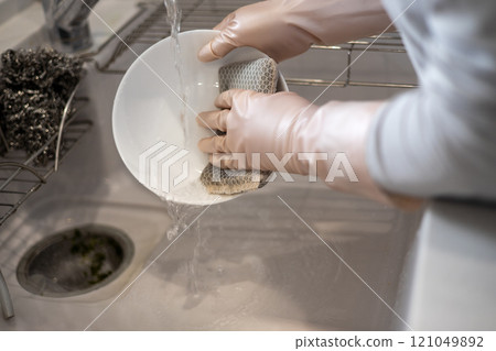 The hands of a woman wearing rubber gloves while washing dishes in the kitchen 121049892