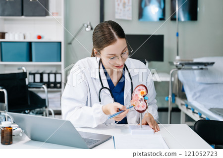 Confident young Caucasian female doctor in white medical uniform sit at desk working on computer. Smiling use laptop write in medical journal in clinic. Confident young Caucasian female doctor in white medical uniform sit at desk working on computer. Smiling use laptop write in medical journal in clinic. 121052723