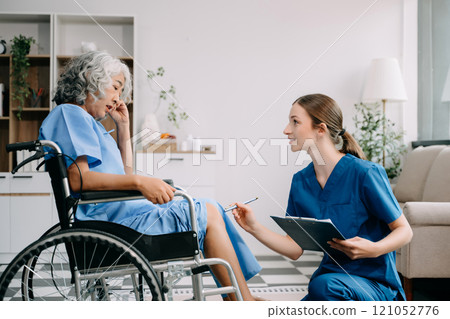 Young nurse helping elderly woman walk in the room, holding his hand, supporting. Treatment and rehabilitation after injury in assisted living facility, senior care Young nurse helping elderly woman walk in the room, holding his hand, supporting. Treatment and rehabilitation after injury in assisted living facility, senior care 121052776