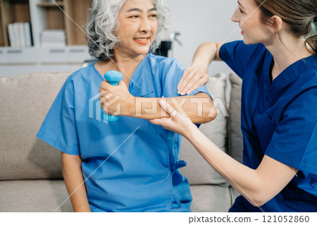 Physiotherapist helping elderly woman patient stretching arm during exercise correct with dumbbell in hand during training hand in hospital in clinic Physiotherapist helping elderly woman patient stretching arm during exercise correct with dumbbell in hand during training hand in hospital in clinic 121052860