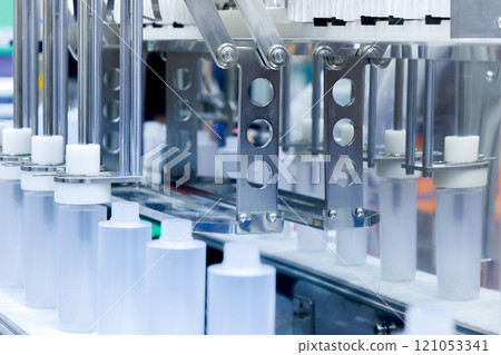 robot arm moving plastic bottle to conveyor belt of auto capping and labeling machine at cosmetic and skin care manufacturing. cosmetic industry and ai technology machinery concept. 121053341