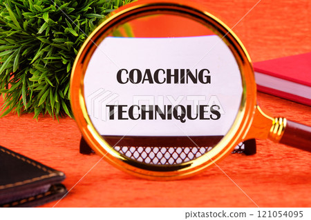 Concept of business and development. Conceptual text COACHING TECHNIQUES written on a white card on an orange background through a magnifying glass 121054095