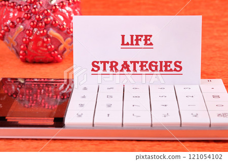 Business and technology concept. The conceptual phrase LIFE STRATEGIES written on a business card on a calculator in front of an orange background Business and technology concept. The conceptual phrase LIFE STRATEGIES written on a business card on a calculator in front of an orange background 121054102